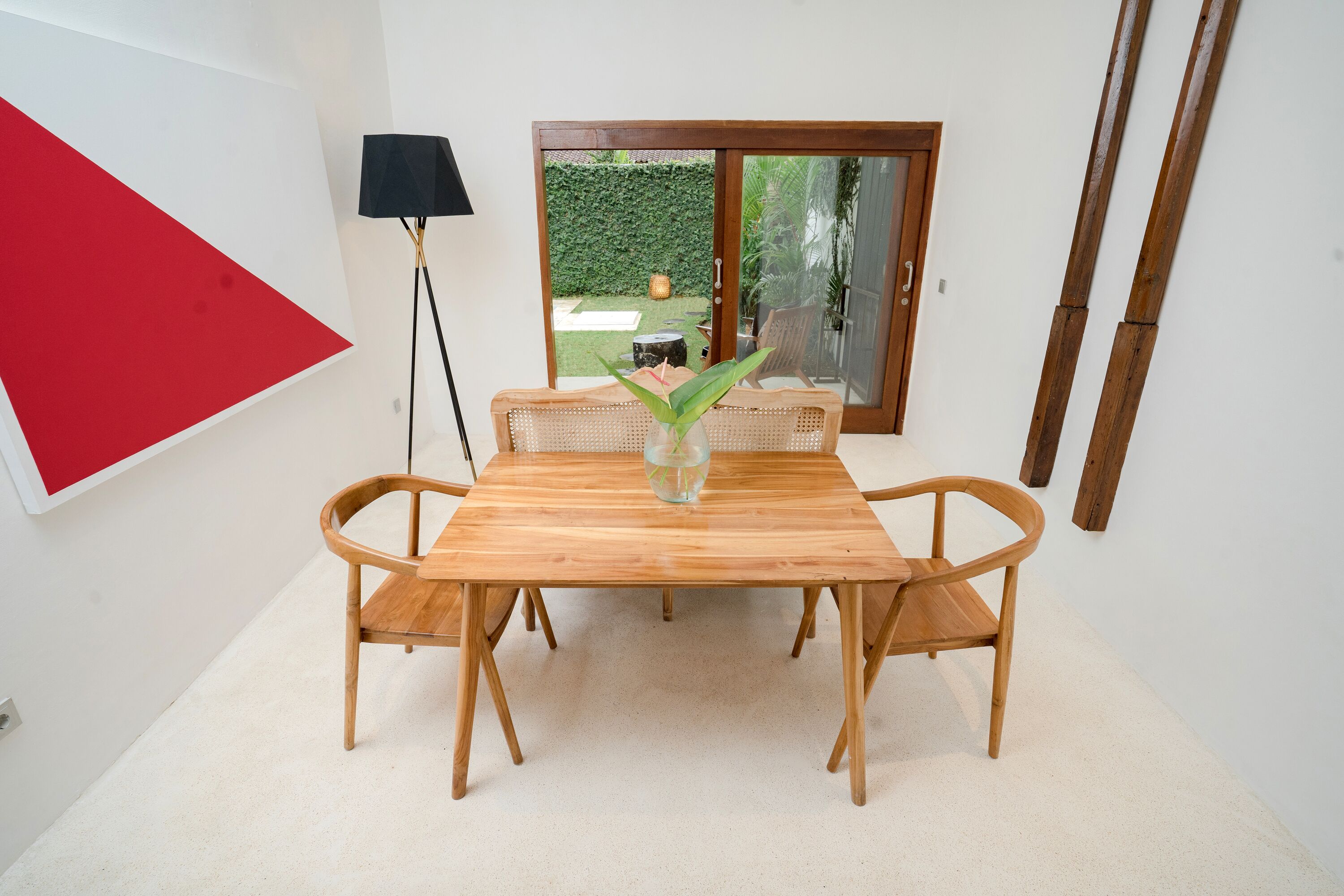 Ein Essbereich mit einem Holztisch und Stühlen, einer Vase mit einer Pflanze und Blick durch eine Glastür in einen Garten.