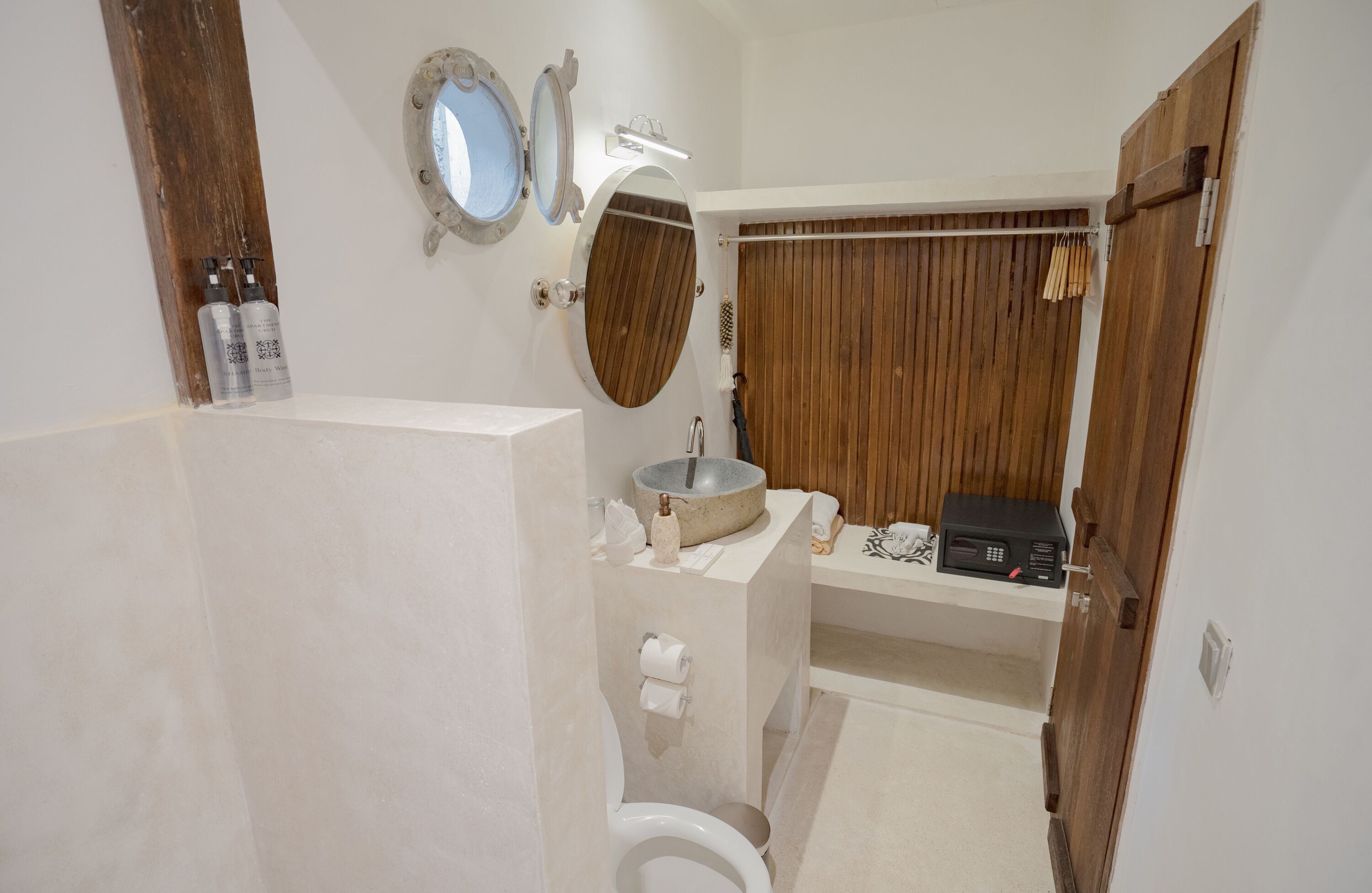 A bathroom with a toilet, sink, and shower area. There are two bottles of hand soap on the wall, a towel rack, and a wooden door.