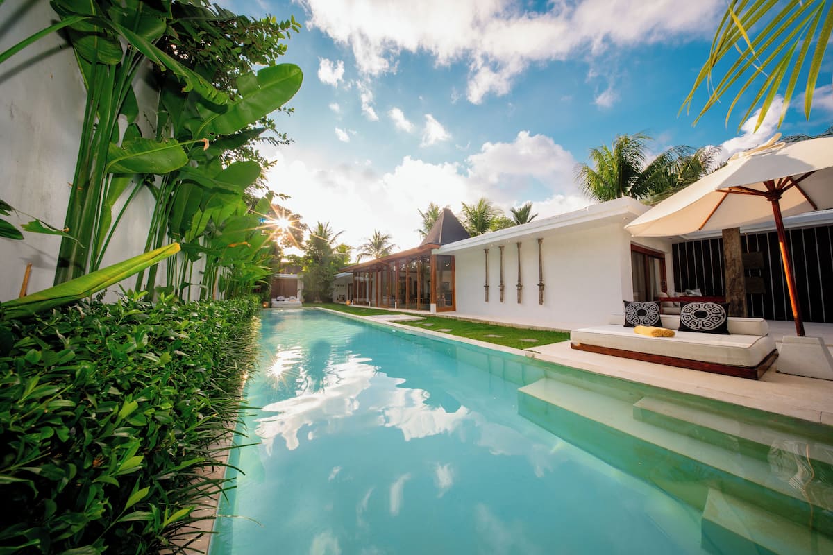 A swimming pool with a clear blue water, surrounded by lush greenery and a white building with columns.