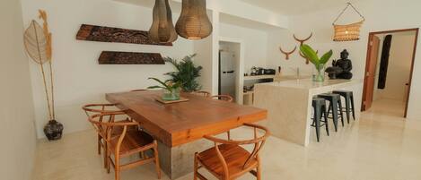 A modern kitchen with a wooden dining table and chairs, a hanging light fixture, and a small island with stools.