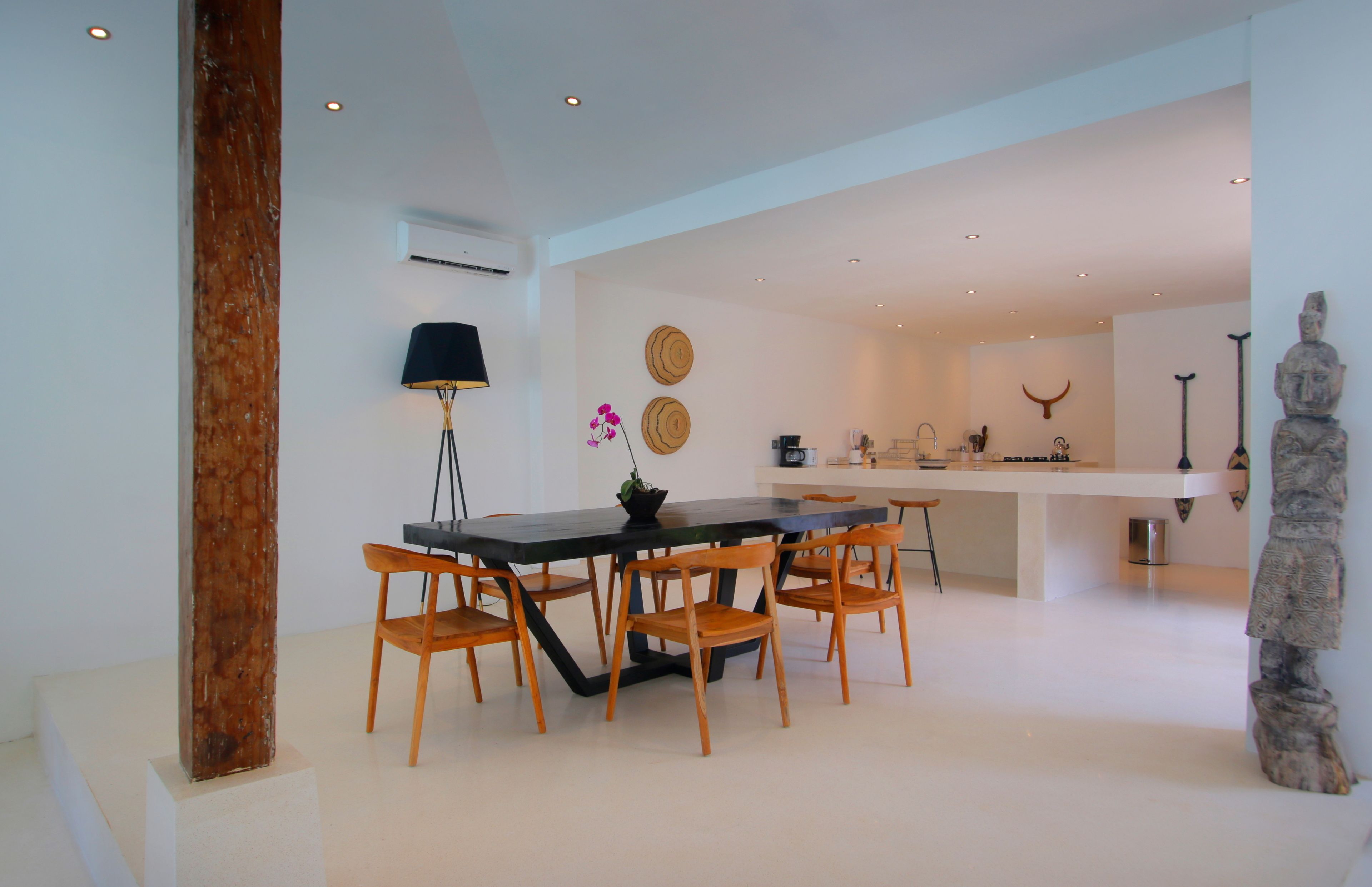 A modern dining area with a long table and wooden chairs, a black floor lamp, and decorative wall art.