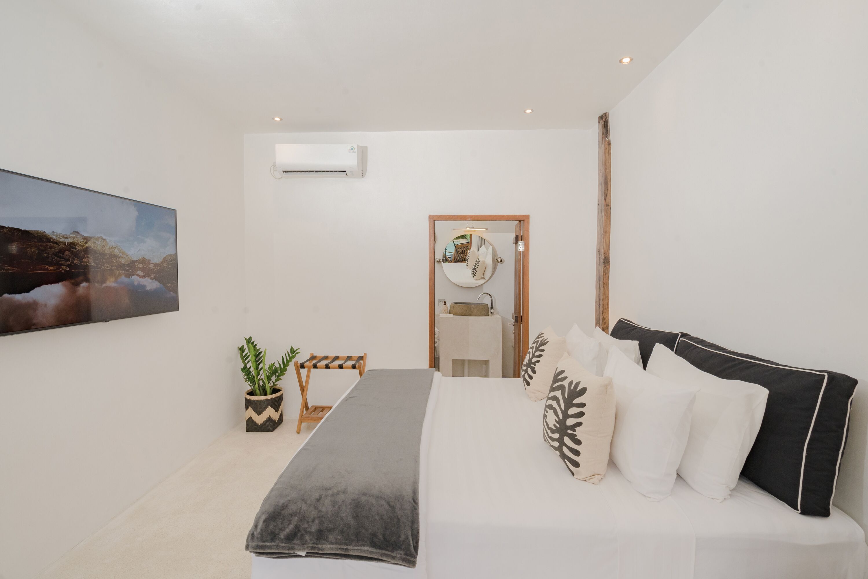 A modern bedroom with a large bed, a bedside table, a potted plant, and a wall-mounted air conditioner.