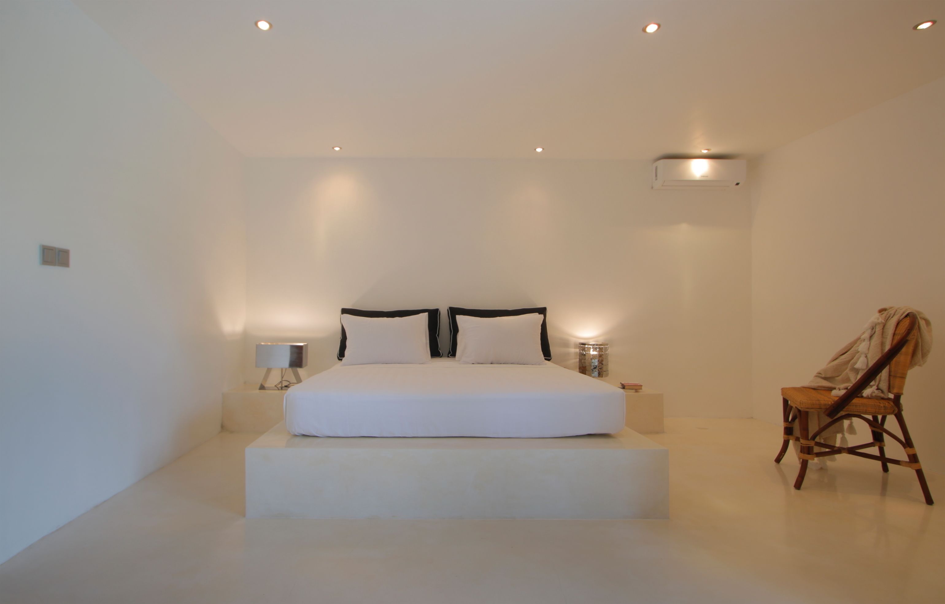 Un dormitorio minimalista con una cama grande, lámparas de noche y una silla.
