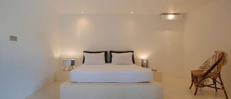 Een minimalistisch slaapkamer met een groot bed, bedlampjes en een stoel.