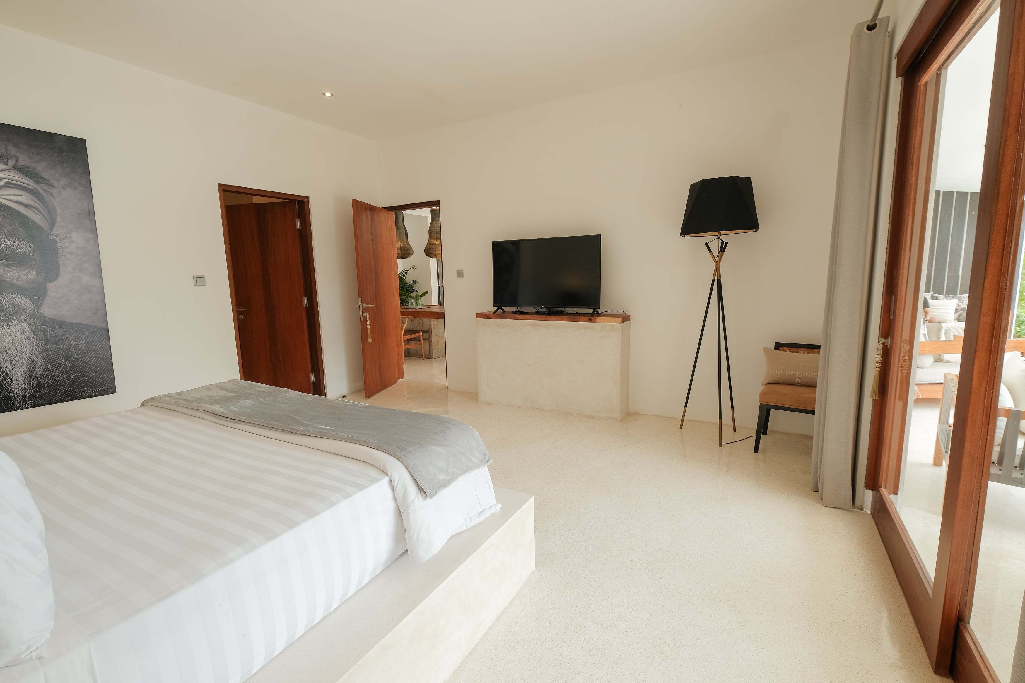 A bedroom with a bed, a television, a floor lamp, and a sliding door leading to a balcony.