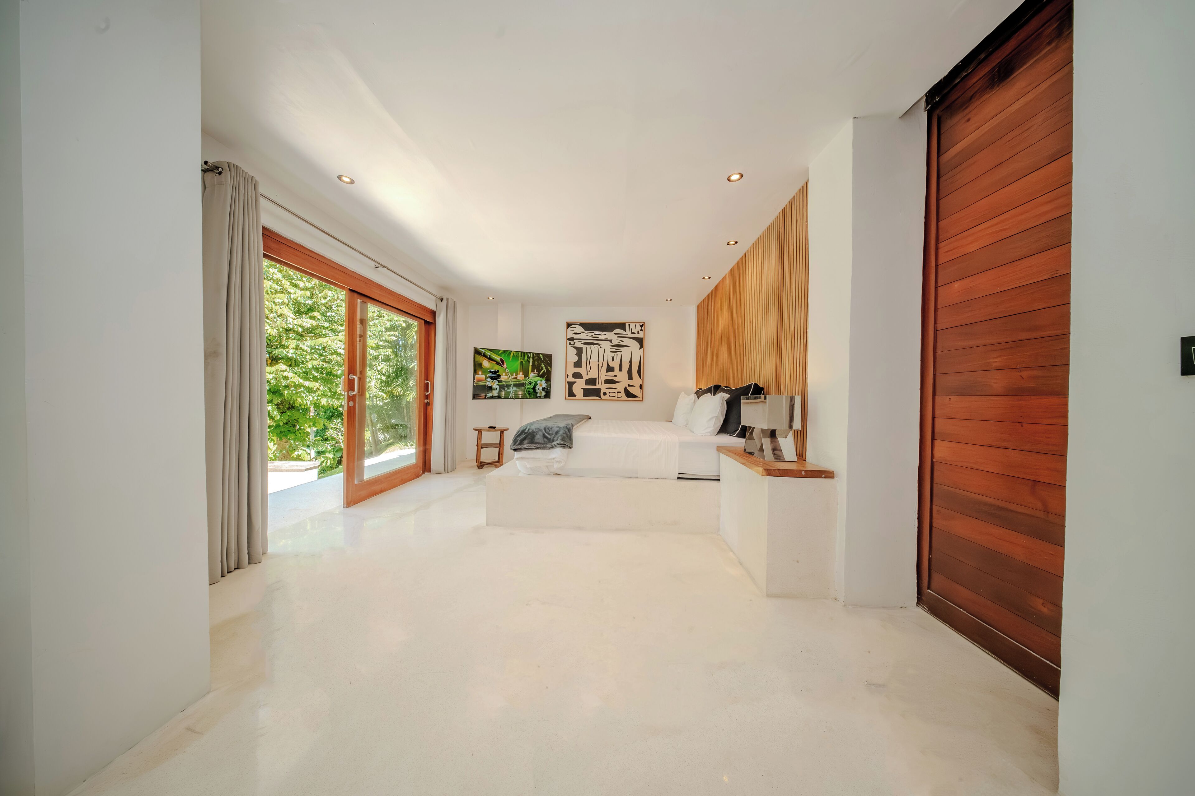 A spacious hallway with a bed, a wooden door, and a large window.