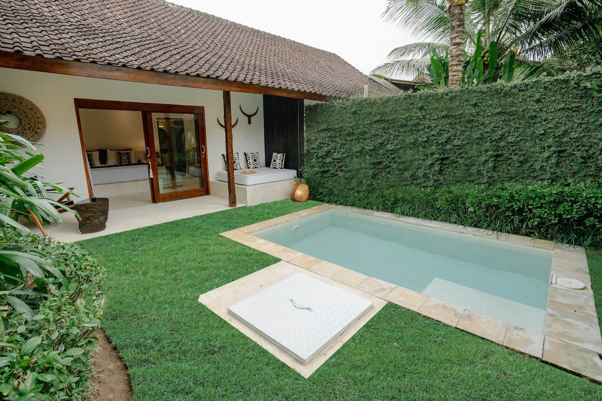 A pool area with a tiled roof, a seating area with cushions, and a well-maintained lawn.