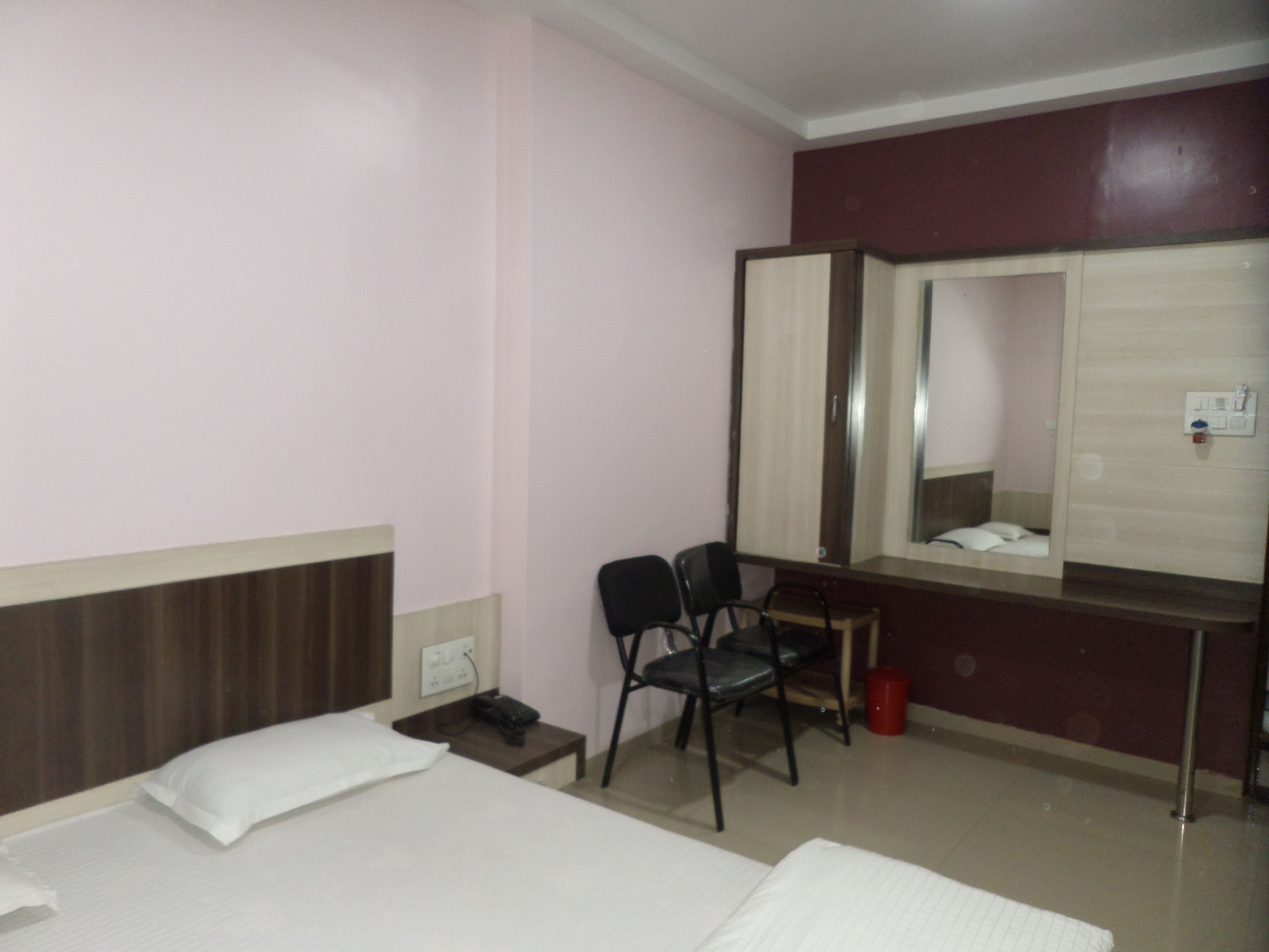 Habitación de hotel con dos camas, un escritorio, una silla, un espejo y un cubo de basura rojo.