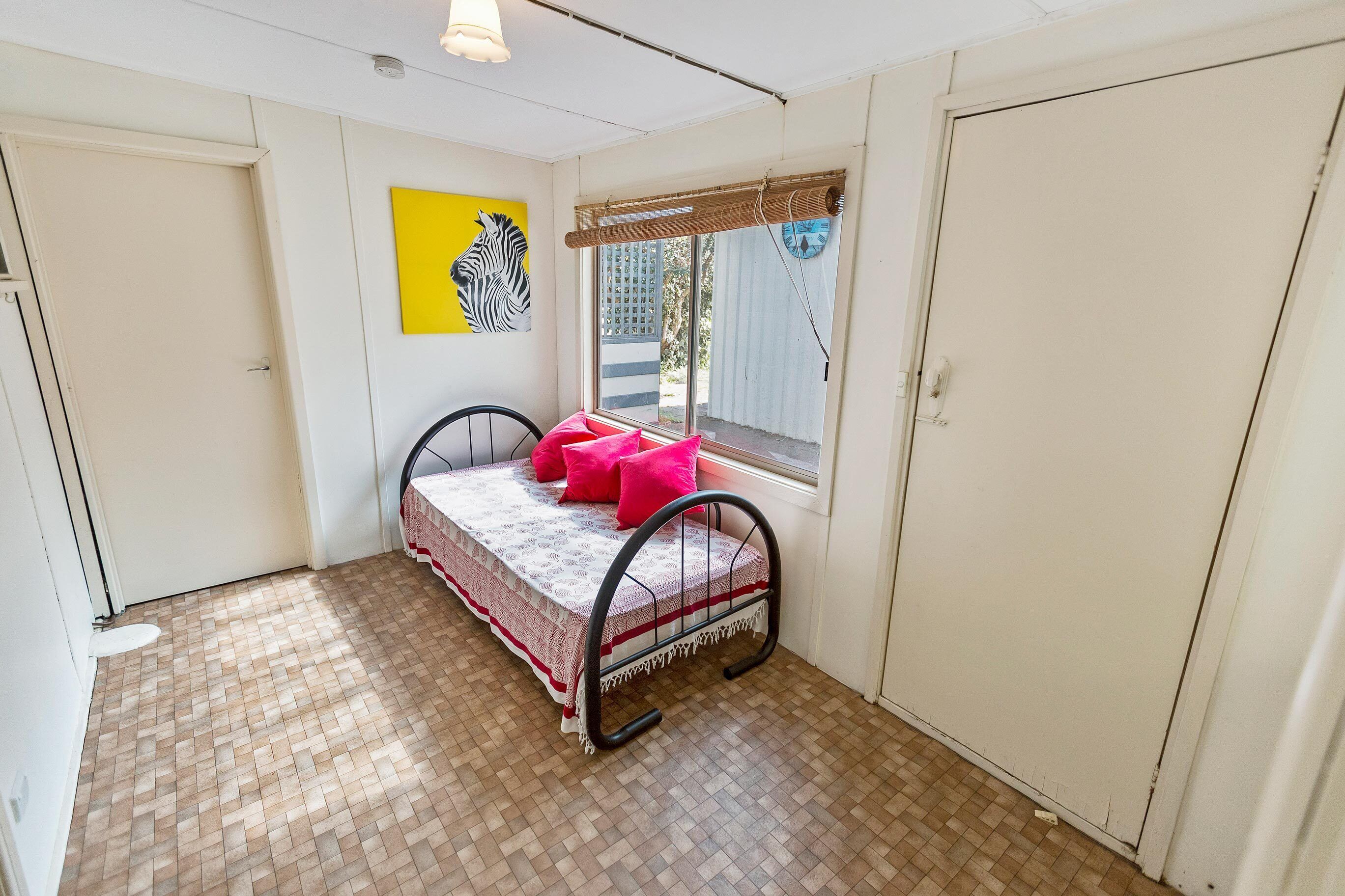 Une petite chambre à coucher, bien rangée, avec un lit, une fenêtre donnant sur un beau paysage et un tableau représentant un zèbre accroché au mur.