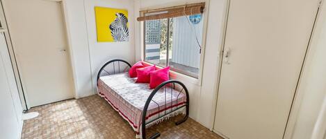 Une petite chambre à coucher, bien rangée, avec un lit, une fenêtre donnant sur un beau paysage et un tableau représentant un zèbre accroché au mur.