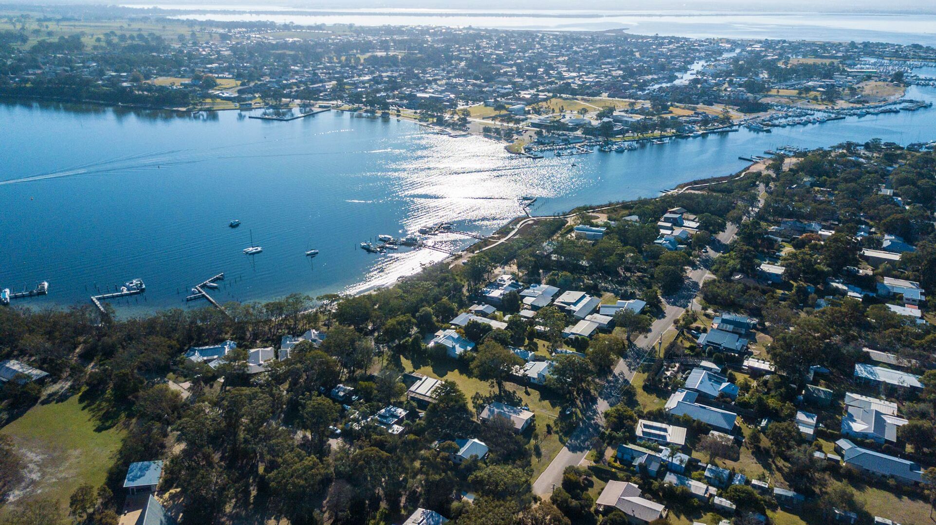 Vista aérea de una zona residencial costera con casas, un puerto deportivo y una gran masa de agua.