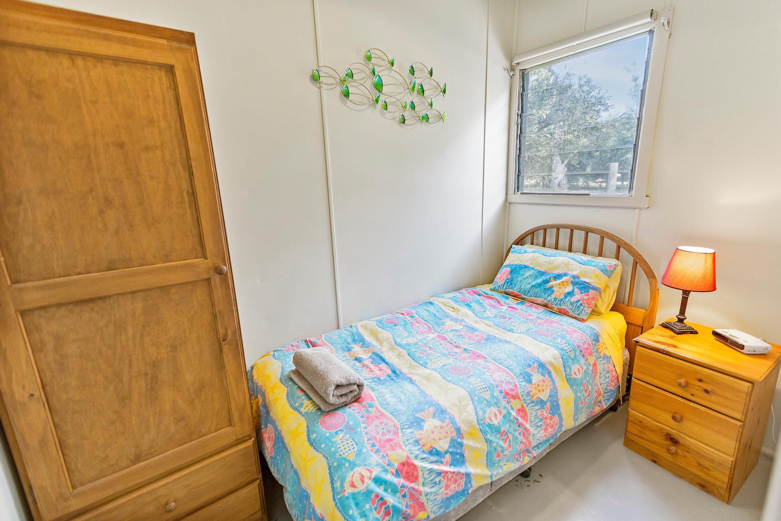 Une chambre à coucher comprenant un lit, une table de chevet, une lampe, une fenêtre et un élément décoratif mural.