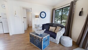 Un salon avec un canapé, un panier décoratif, une valise ancienne et une horloge au mur.
