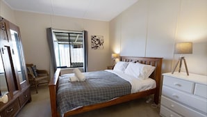 Une chambre à coucher bien rangée, avec un lit en bois, une commode blanche, un miroir et une fenêtre avec des rideaux.