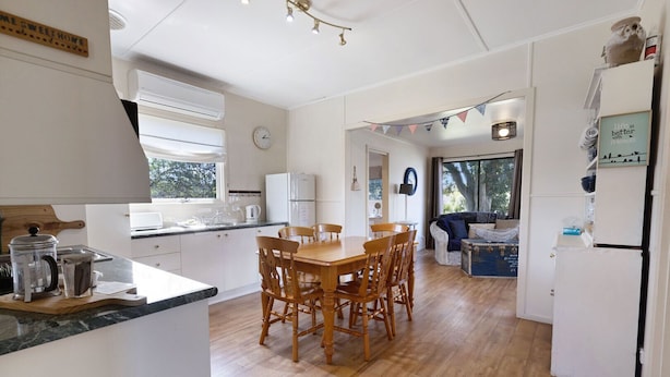 Une cuisine moderne avec une table et des chaises en bois, des meubles blancs et une vue sur l’extérieur.