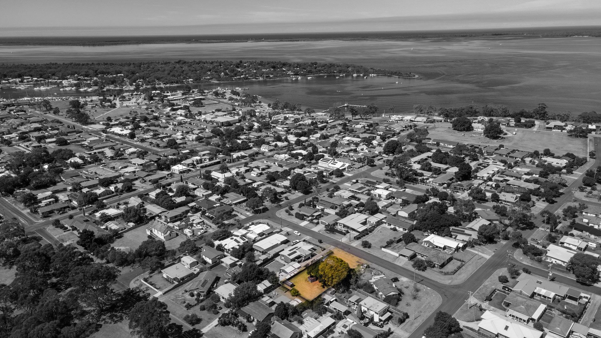 An aerial view of a residential area with houses, roads, and a large body of water in the background.