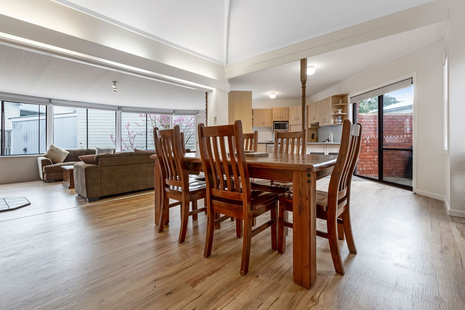 A spacious living area with a dining table and chairs, a sofa, and a kitchen in the background.