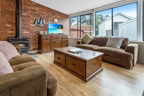 A living room with a brick wall, a fireplace, a sofa, a coffee table, and a television.