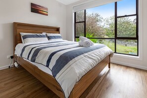 A bedroom with a wooden bed, a large window, and a painting on the wall.