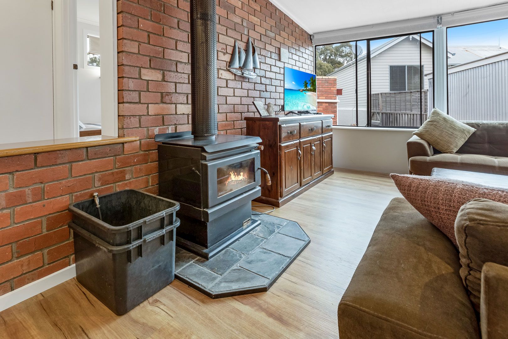 A living room with a brick fireplace, a television mounted on the wall, and a sofa.
