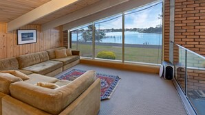 Una habitación amplia con un gran ventanal con vistas a un lago, un sofá color beige y una alfombra estampada.