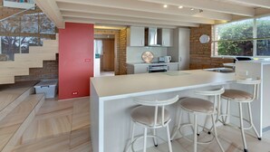 Una cocina moderna con una isla central, taburetes de bar y una puerta roja que da a una escalera.