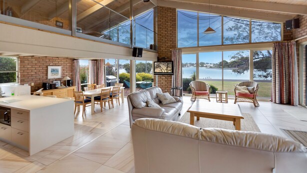 Amplia sala de estar con un ventanal grande con vista a un cuerpo de agua, una cocina con comedor y una zona de estar acogedora con sofá y sillones.