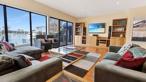 A spacious living room with large windows, a flat-screen TV, and a view of a marina.