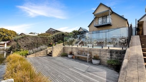 A modern house with a wooden deck, a glass conservatory, and a stone staircase.