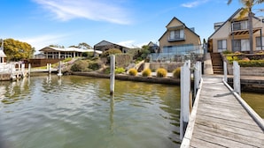 A waterfront property with a wooden dock, a house with a large balcony, and a staircase leading to a second level.