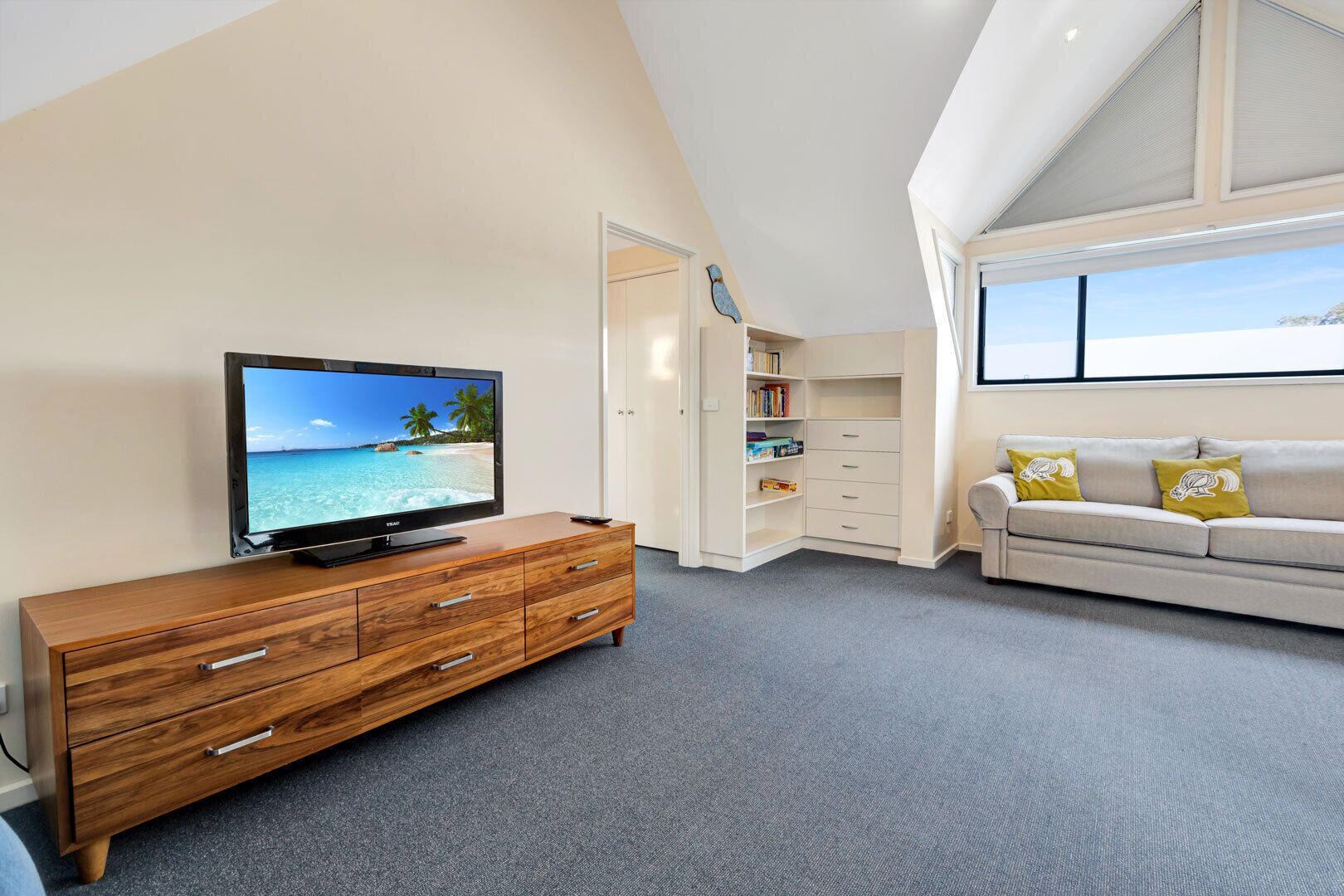 Una sala de estar moderna con televisor de pantalla plana, un mueble de madera, estanterías y un sofá con cojines.