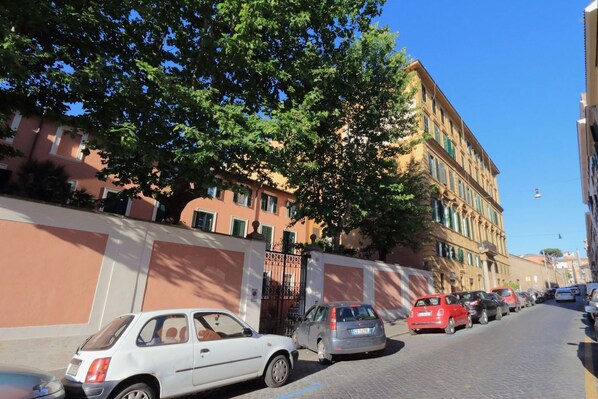 A street with parked cars and a building with a large tree in front.