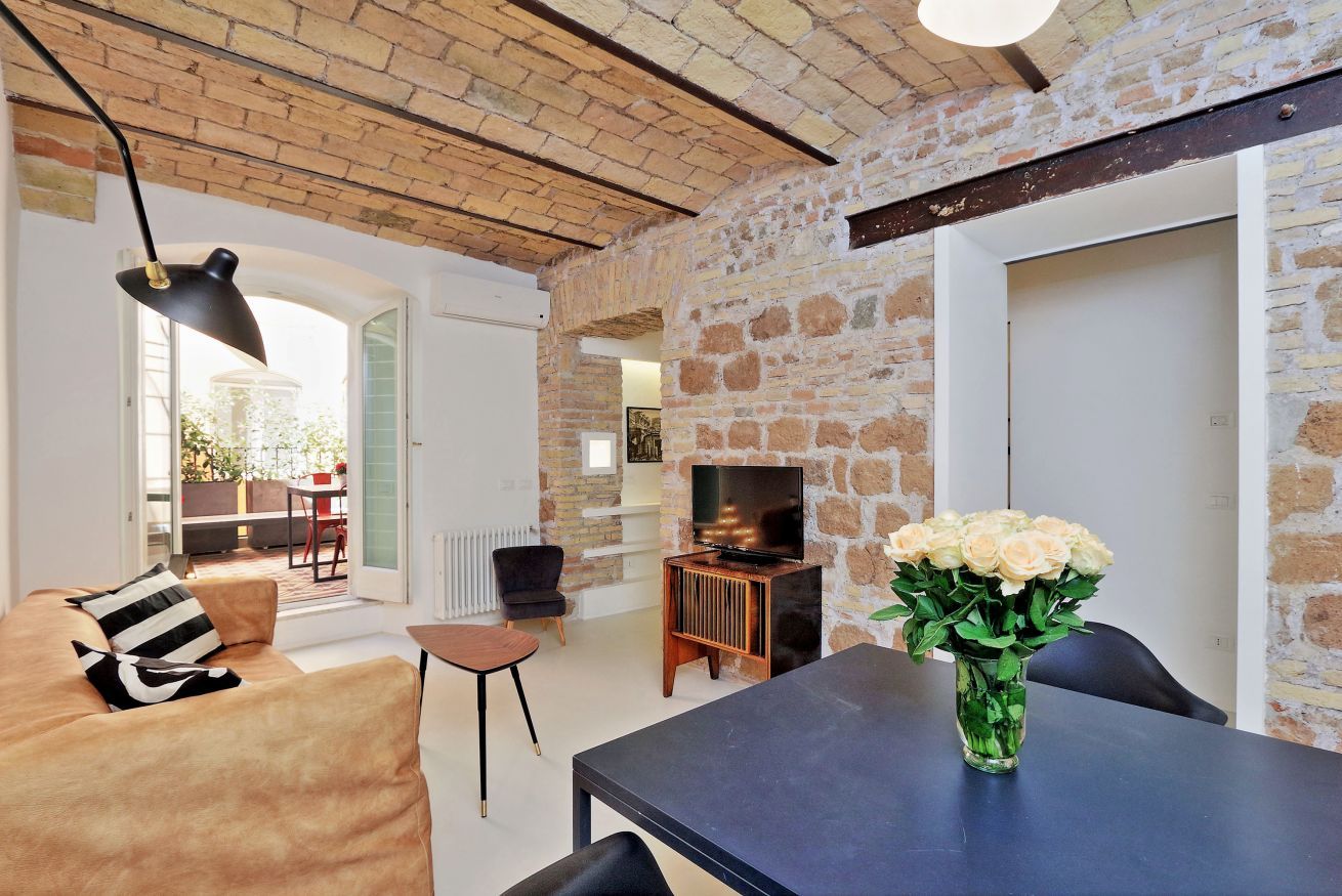 A modern living room with a stone wall, a sofa, a coffee table, a TV, and a vase of flowers.