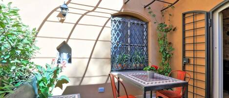 Un piccolo patio esterno con tavolo e sedie, circondato da piante e un muro decorativo.