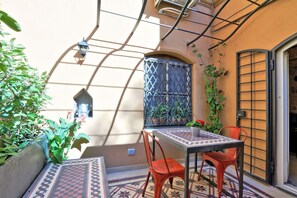 A small outdoor patio with a table and chairs, surrounded by plants and a decorative wall.