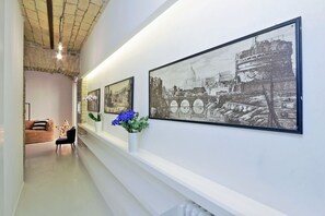 A hallway with framed black and white photographs on the wall, a white vase with blue flowers, and a sofa with a star-shaped light decoration.