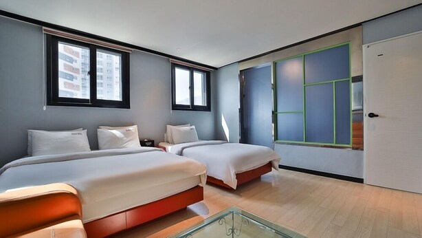 Une chambre d’hôtel moderne avec deux lits, une table basse en verre et de grandes fenêtres équipées de stores.
