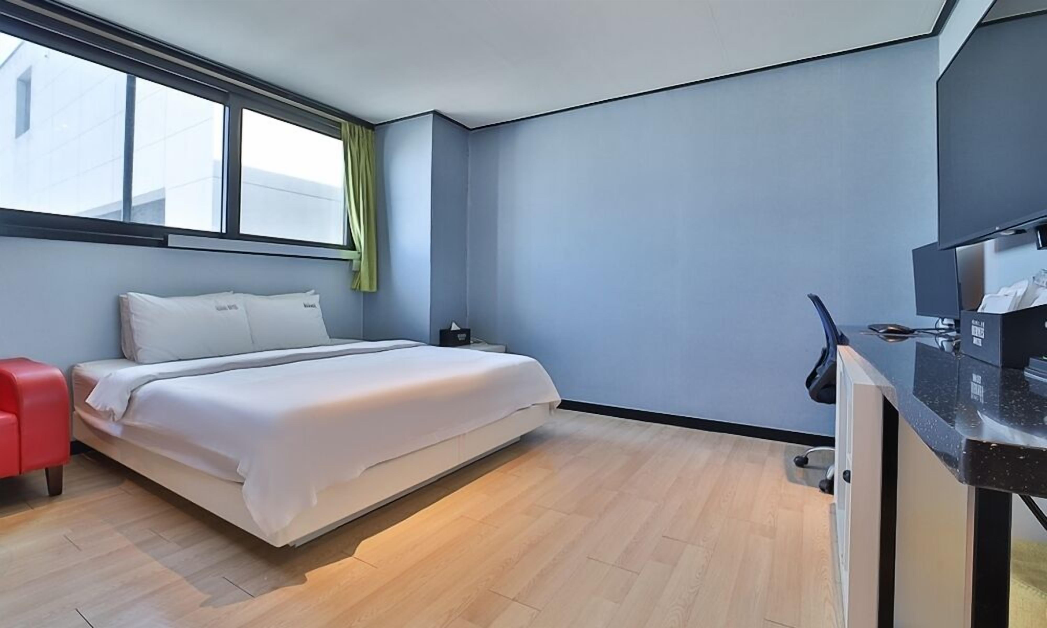 A modern hotel room with a bed, a desk, and a window with curtains.