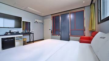 A hotel room with a bed, a desk, a chair, a mirror, and a window with curtains.