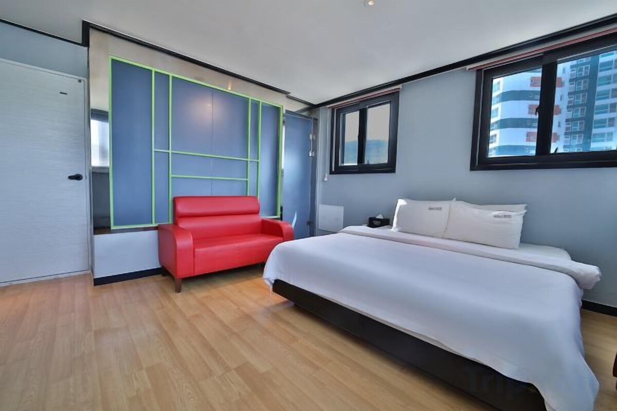 A bedroom with a bed, a red chair, a window, and a door.