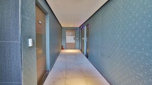 Un couloir aux murs ornés de motifs, doté d’un sol carrelé et de portes sur lesquelles figurent les numéros des chambres.