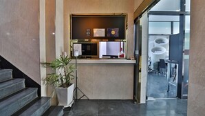 Un comptoir d’accueil agrémenté d’une plante, un panneau indiquant les numéros des chambres et une porte vitrée donnant sur un espace détente.