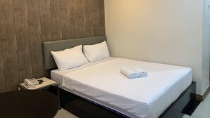 A hotel room with a bed, a bedside table with a phone, and a wooden accent wall. - Maine City (Manila)