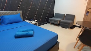 A hotel room with a bed, two armchairs, a small table, and a desk with a chair. - Maine City (Manila)