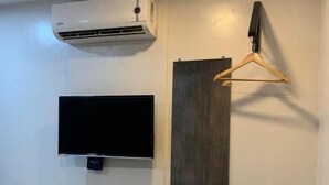 A room with a mounted air conditioner, a flat-screen TV, a wooden hanger, and a mirror reflecting a bed. - Maine City (Manila)