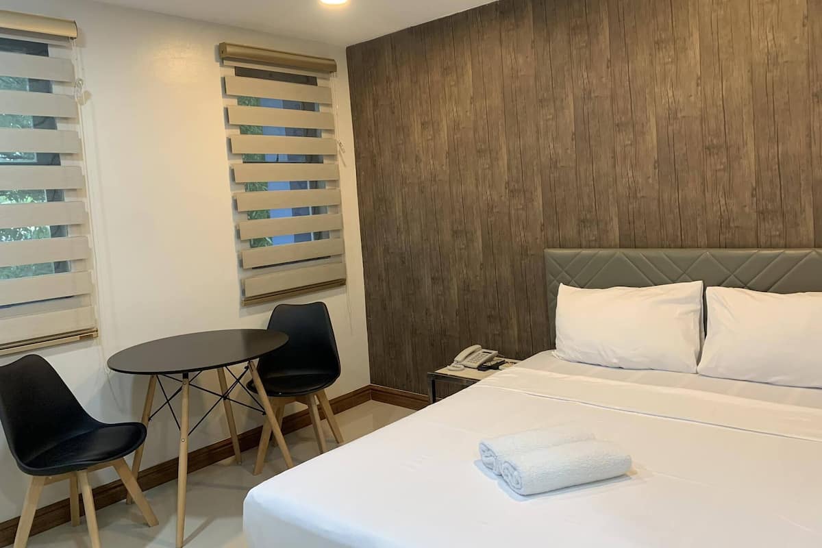 A hotel room with a bed, two chairs, a small table, a phone, and a window with blinds.