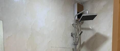 Un baño con inodoro, ducha con cabezal de ducha manual y grifo empotrado en la pared.