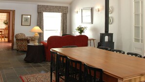 A dining area with a high ceiling, a chandelier, a large window, a fireplace, and a red sofa. - 1A St Aidans Guest House (Makhanda)