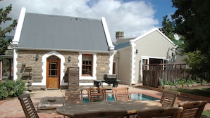 A stone house with a pool, wooden furniture, and a barbecue area. - 1A St Aidans Guest House (Makhanda)