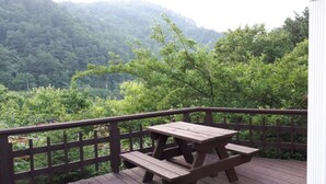 Una terraza de madera con mesas de picnic con vistas a un valle boscoso.